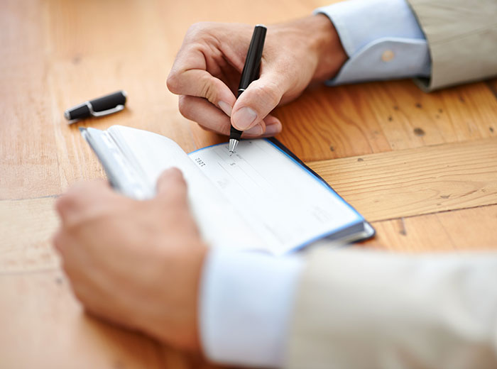 A man filling out a check in a checkbook at a wooden table