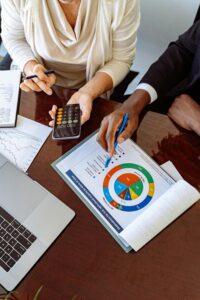 Two people working out loan terms over a table with bar and pie graphs with a calculator and laptop