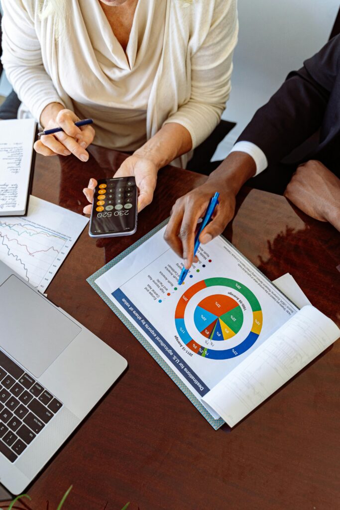 Two people working out loan terms over a table with bar and pie graphs with a calculator and laptop