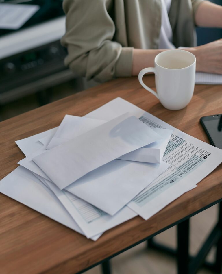 A person sitting at a desk with a cup of coffee and a stack of various forms and paperwork