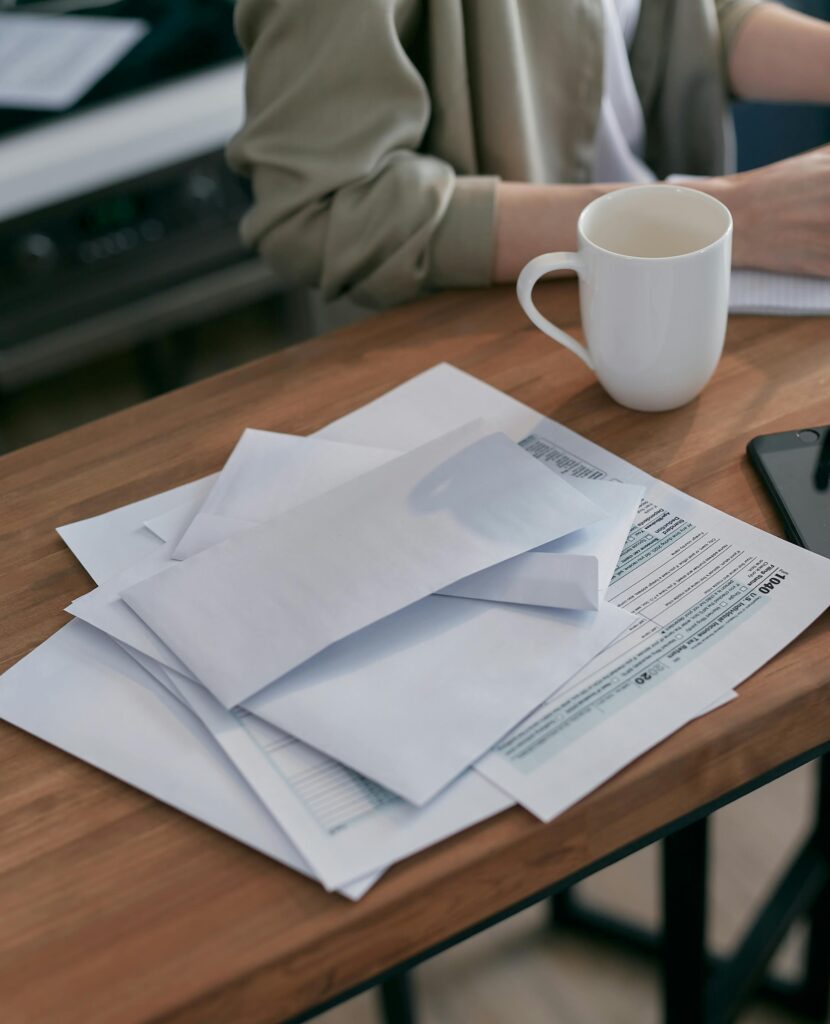 A person sitting at a desk with a cup of coffee and a stack of various forms and paperwork