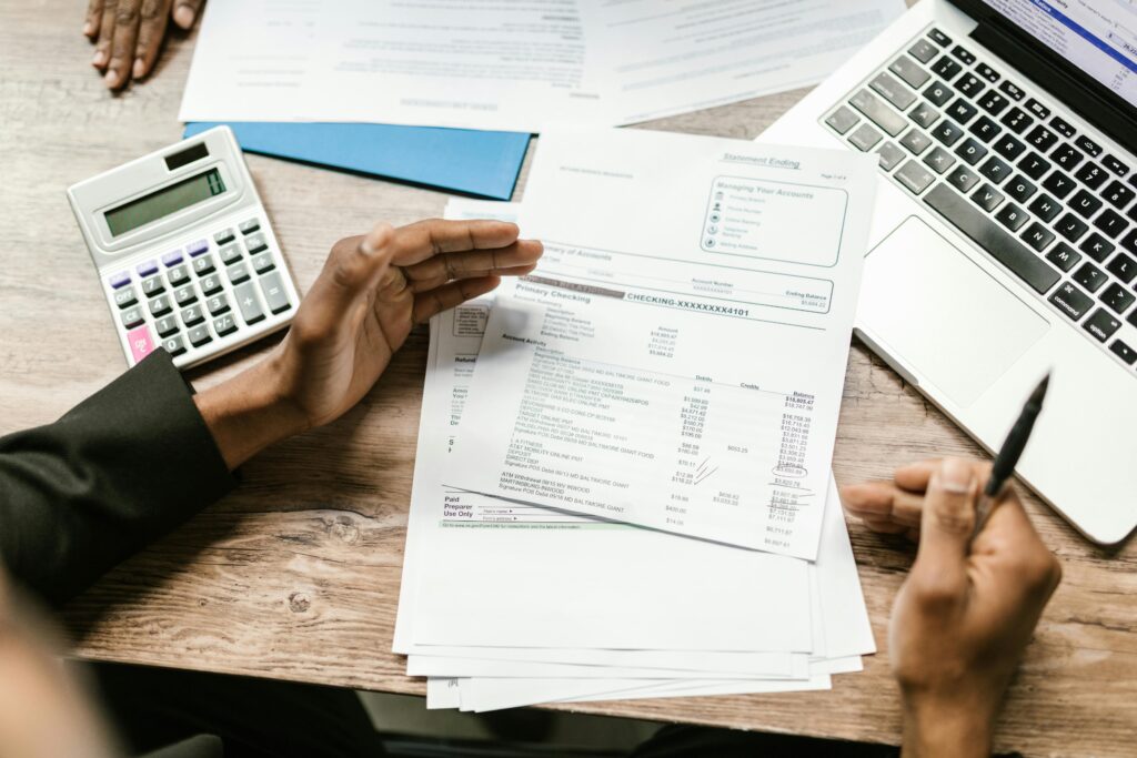 A man balancing his checkbook at a desk with a calculator and laptop